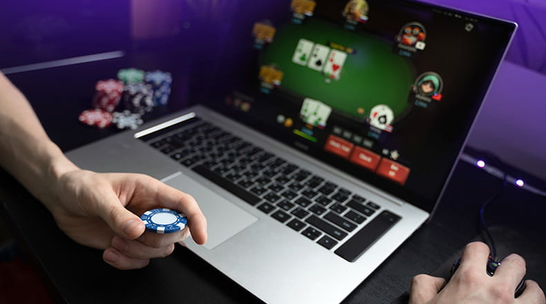 A person playing online poker on a laptop with a blue poker chip in their hand.