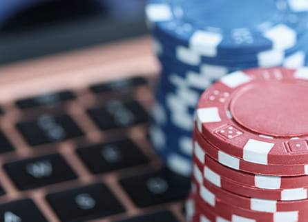 Blue and red casino chips resting on a laptop computer.