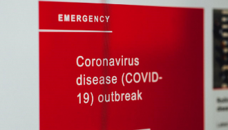 An emergency sign with a red background with Coronavirus disease (COVID-19) outbreak written.