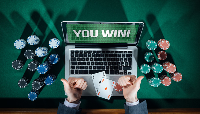 A Man is Celebrating his Win in front of a Laptop, Casino Chips and Playing Cards