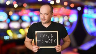 A Person Holding Open to Work Sign with Blurred Casino Hall as a Background
